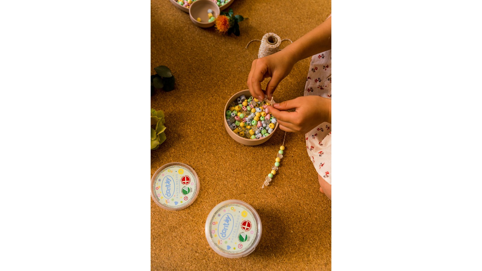 Hænder sorterer små perler i plastikbeholdere på et bord med gylden overflade.